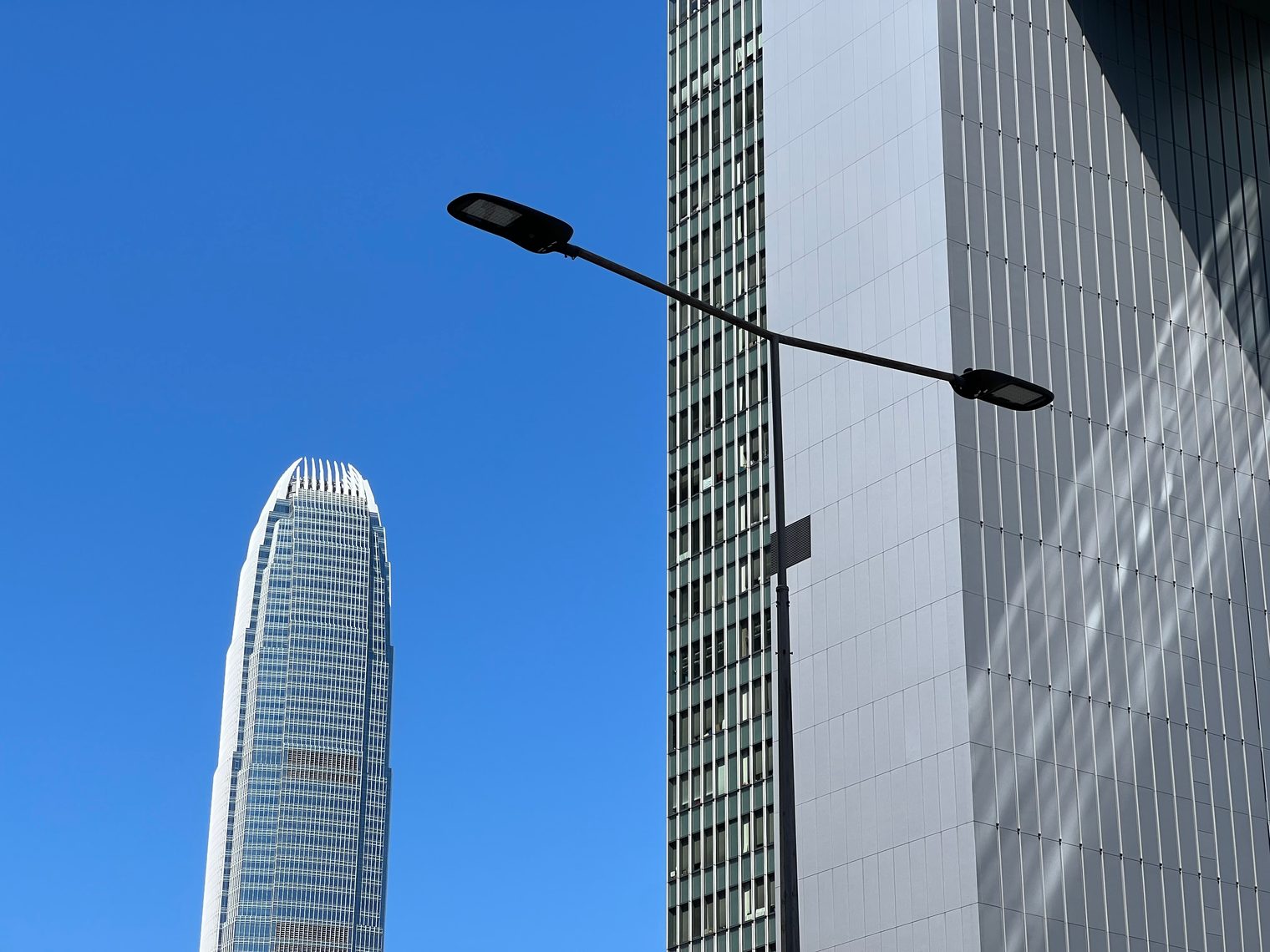 A telephoto shot against a deep blue sky: the crown of Two IFC, a double-headed street lamp and the facade of an office tower
