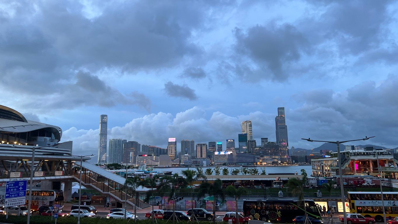 The same spot on an overcast evening, dark clouds over the lit towers across the harbour