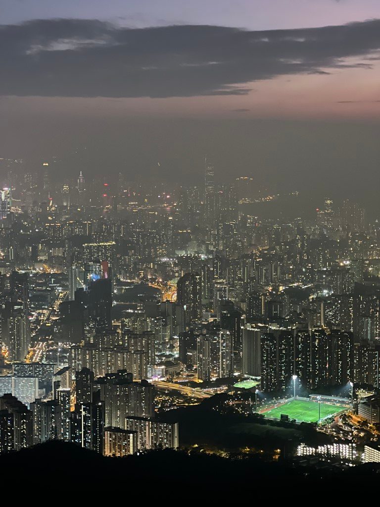 City lights from a hill after dark, with a brightly lit football pitch close by