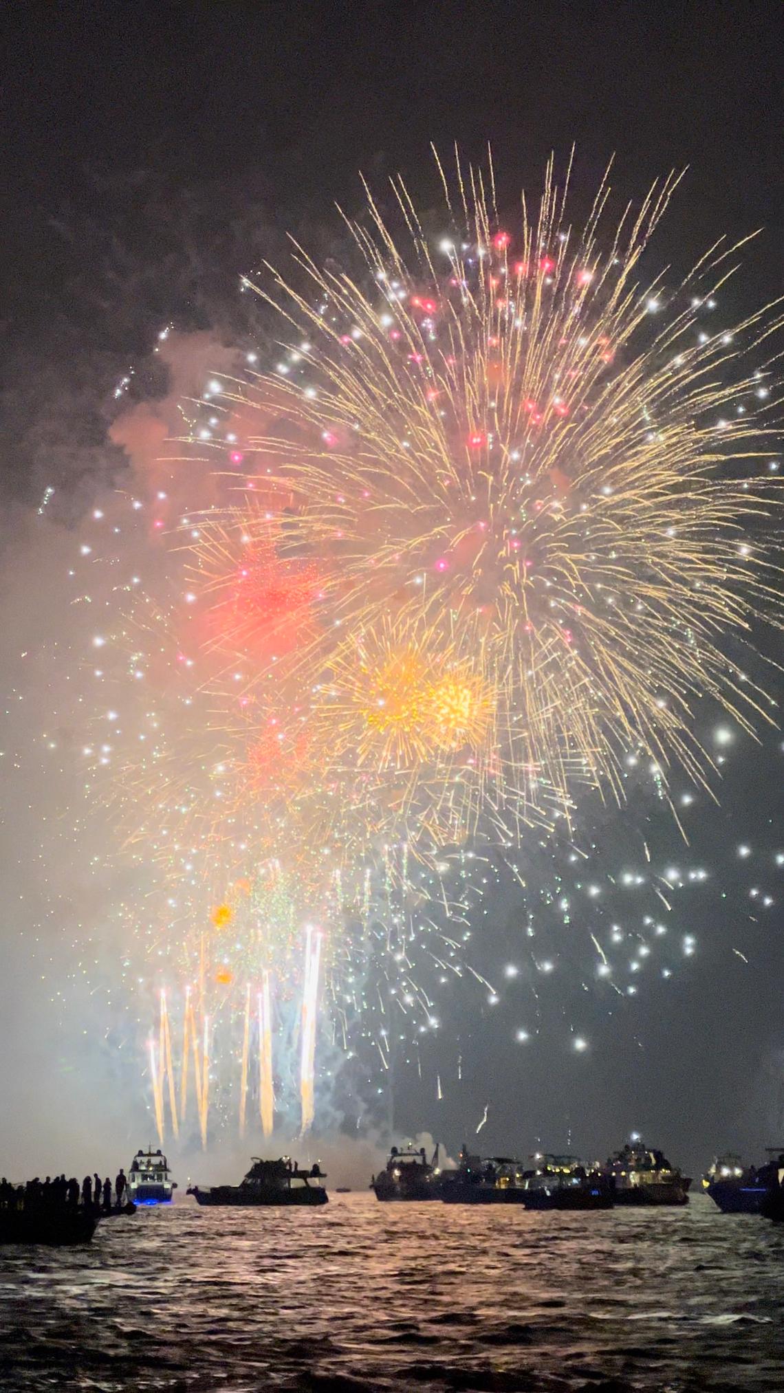 Fireworks bursting over the sea at night, boats full of spectators below
