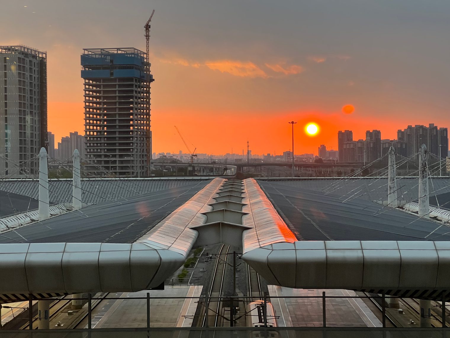 Railway station canopies and tracks leading into the distance, the sun setting between half-built towers