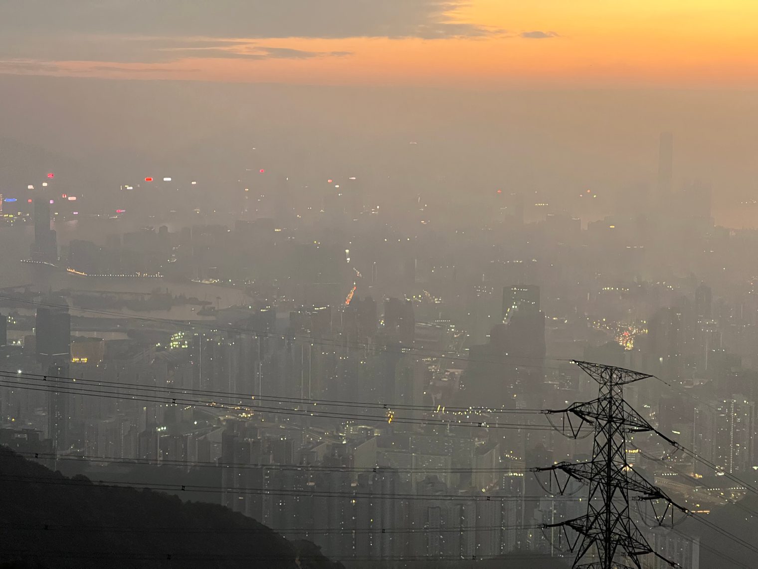 Kowloon from a hill at dusk, the city in haze with its first lights on and a pylon close by