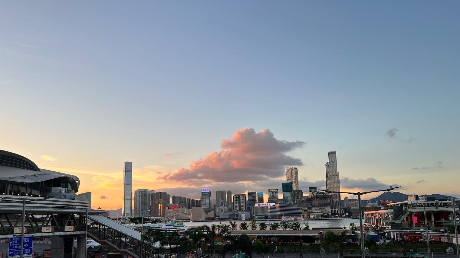 The same spot, a single cloud turned pink by the setting sun resting above the towers in a pale blue sky