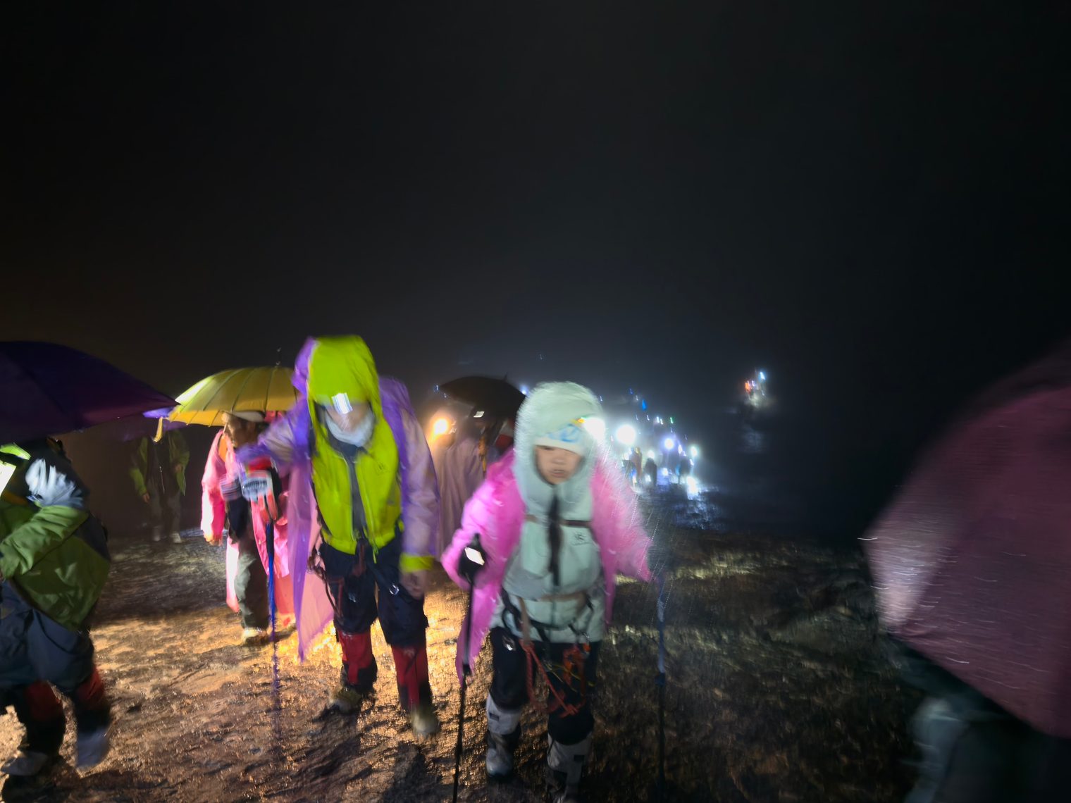 The night summit push: climbers in headlamps and rain gear, a line of lights ahead