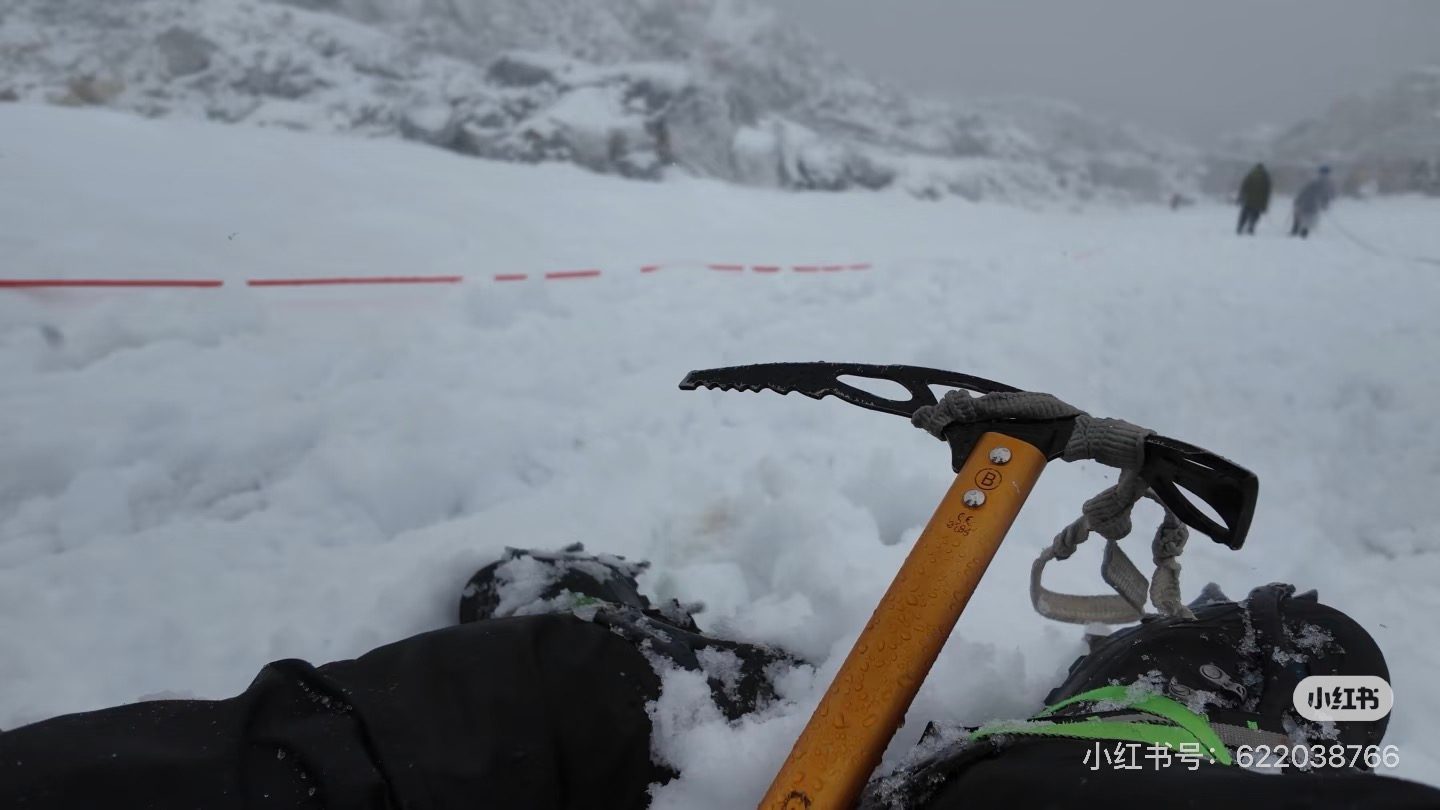 Gloved hands resting on an ice axe planted in the snow, fixed rope running past