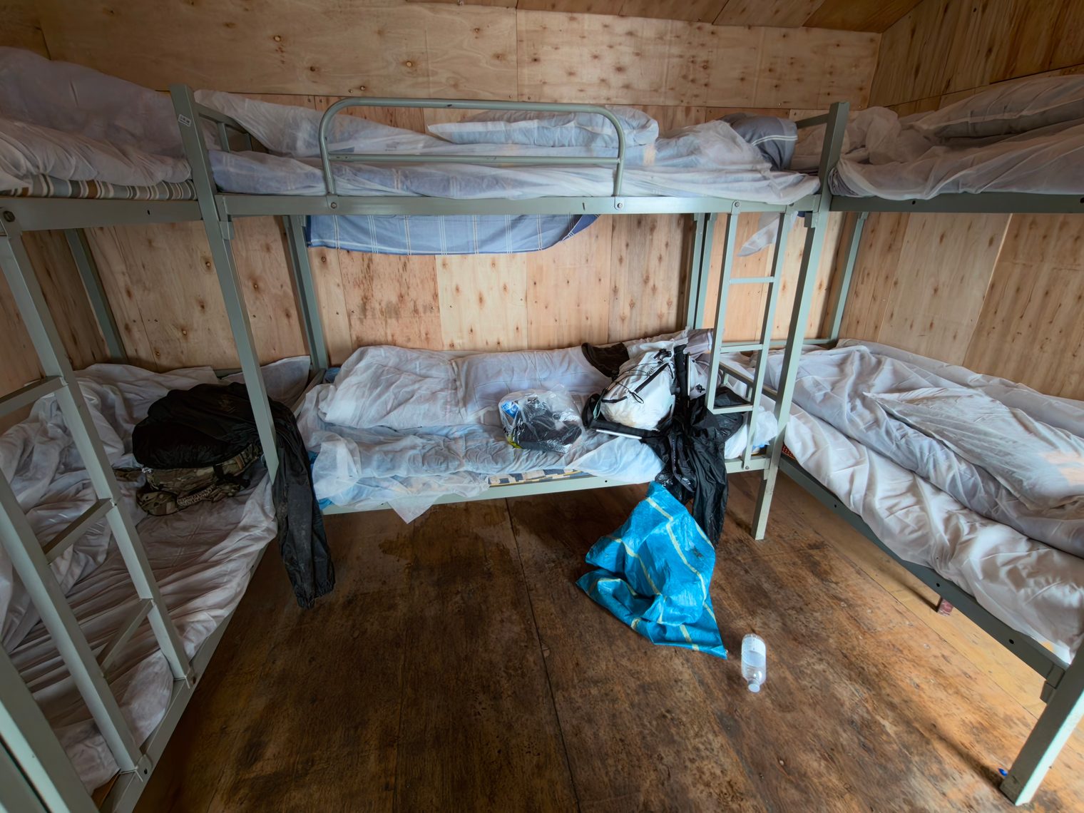 Dormitory interior: metal bunk beds with white quilts in a plywood room