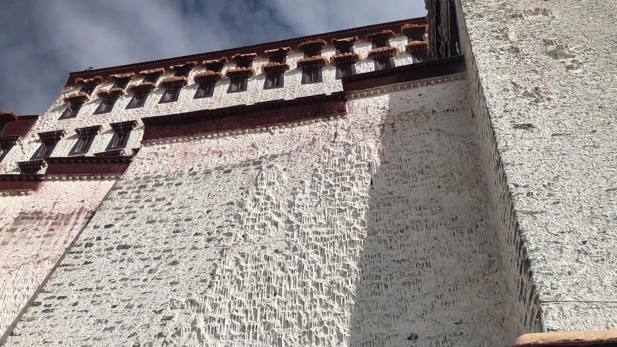 Looking up at a tall white wall: layer on layer of whitewash has run and set into stalactite-like drips, with dark red bands and a row of windows above