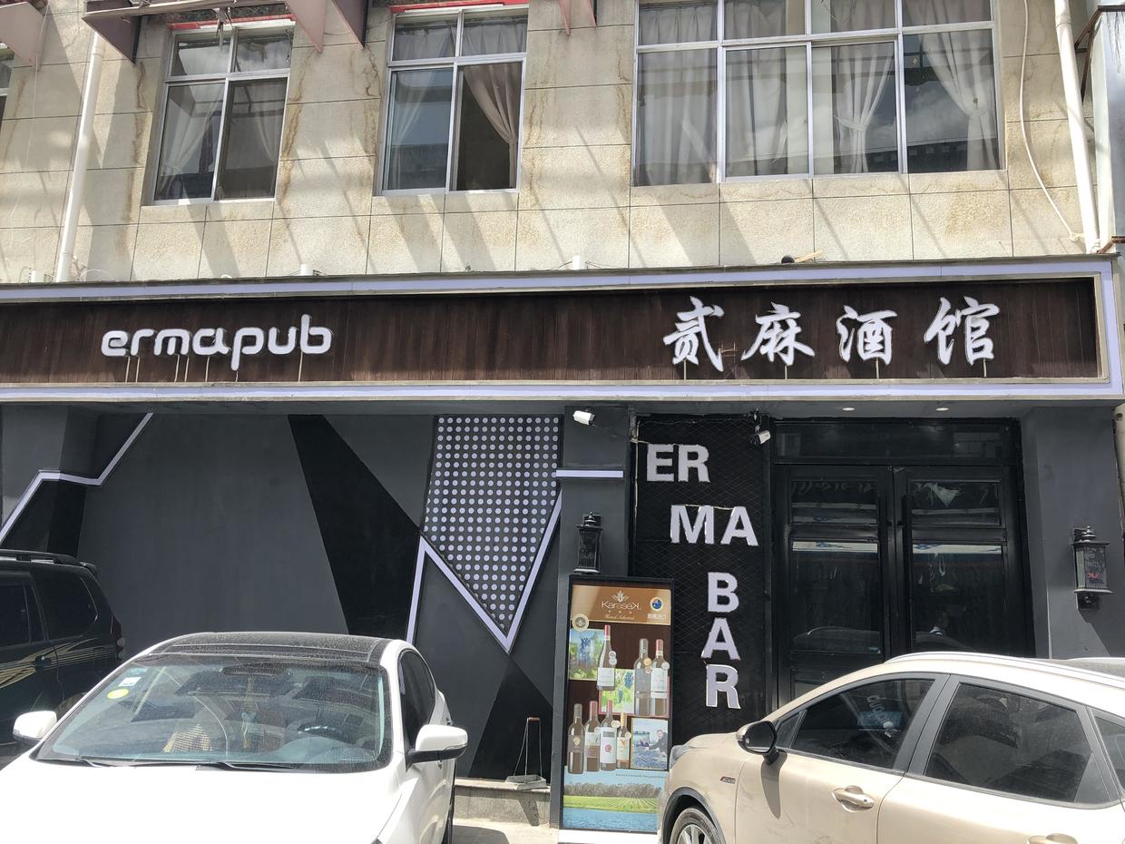The front of a bar in Lhasa called 贰麻酒馆, "ermapub", with two cars parked outside
